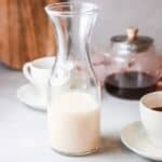 Jug of homemade cashew creamer on table with cup of coffee