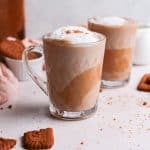 Glass mug of lotus biscoff latte with biscoff biscuits alongside.