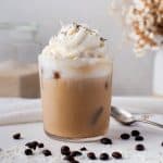 Glass of coconut cold brew coffee topped with whipped cream with coffee beans and shredded coconut next to glass.