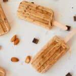 almond mocha popsicles on flat surface surrounded by chocolate chips and whole almonds.