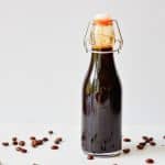 jar of homemade coffee syrup surrounded by loose coffee beans.