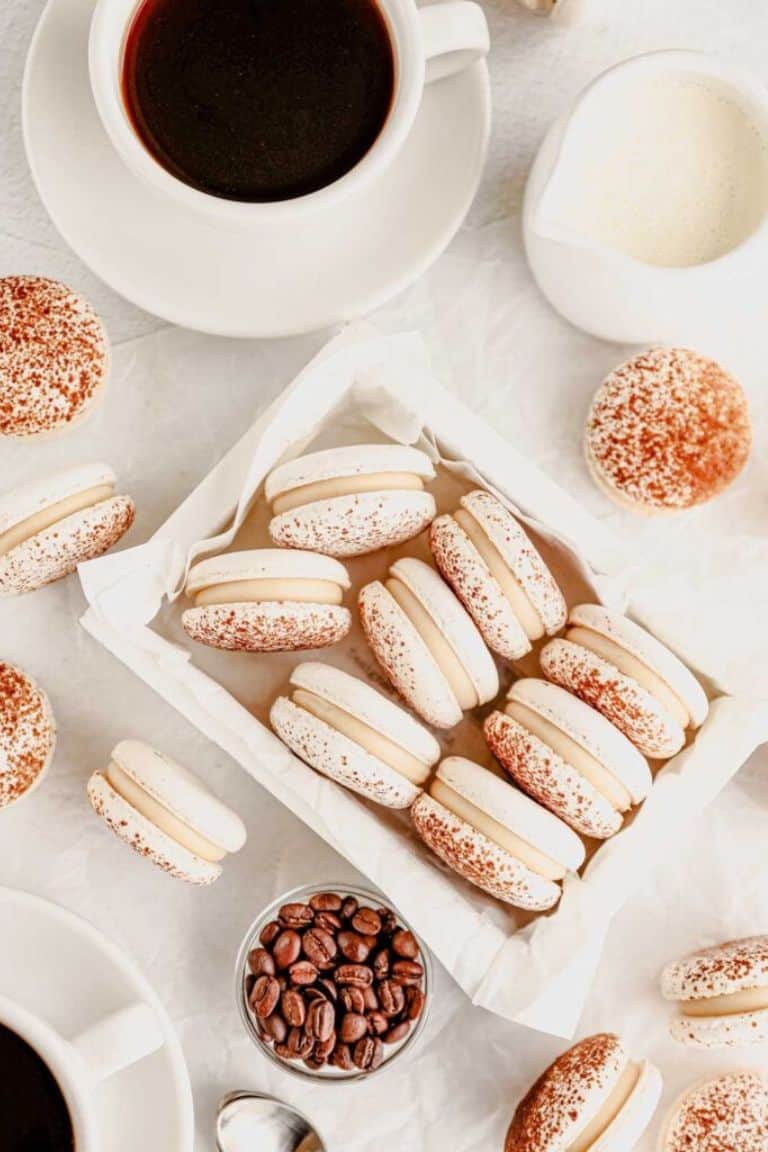 coffee macarons stacked in tray with cups of coffee alongside.
