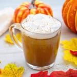 pumpkin spice latte in glass cup with pumpkins and leaves around it.