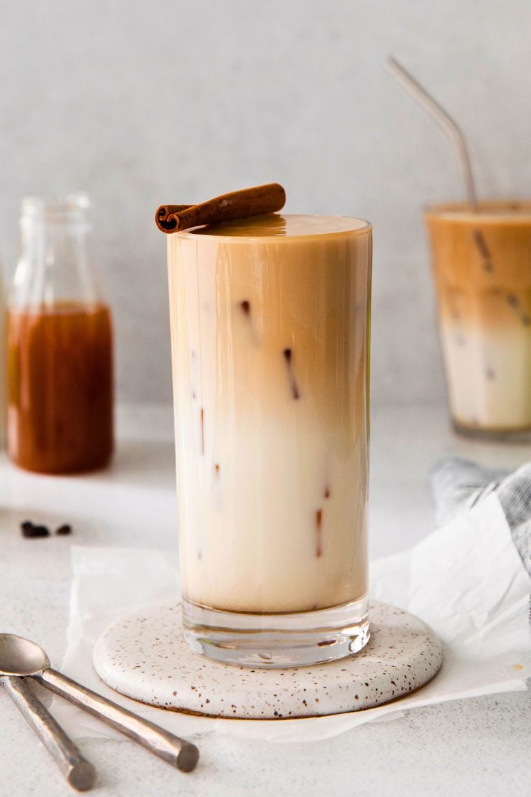 iced apple crisp macchiato topped with cinnamon stick in tall glass.
