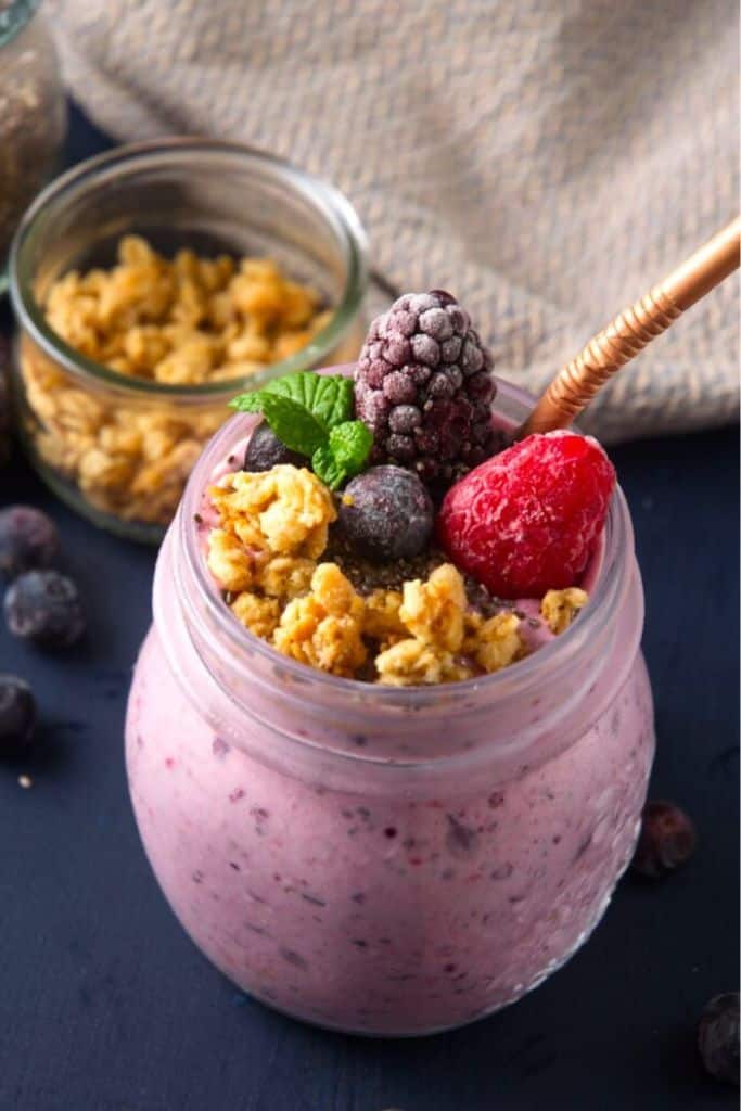 berry chia smoothie in jar with straw and toppings.