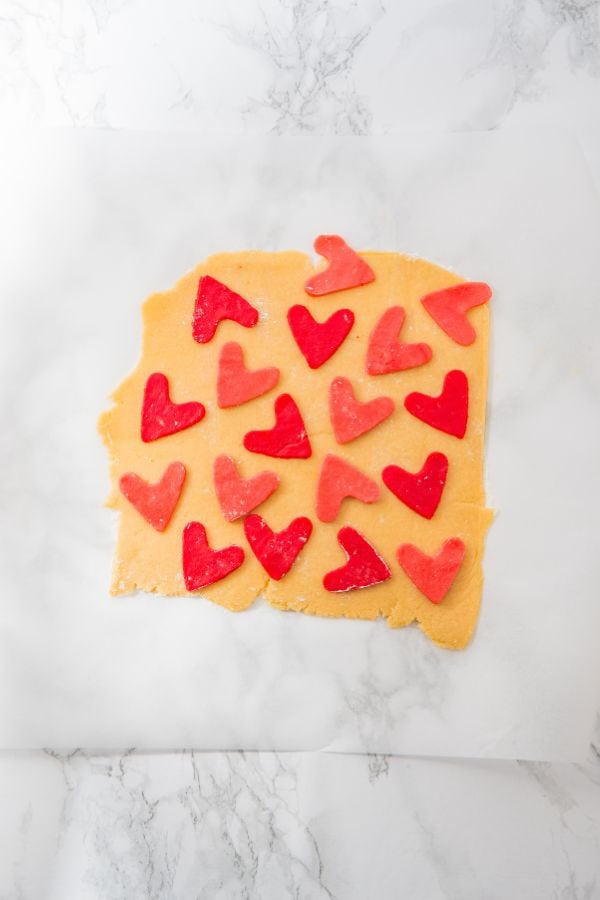 pink heart cut out cookies laid out on rolled cookie dough.