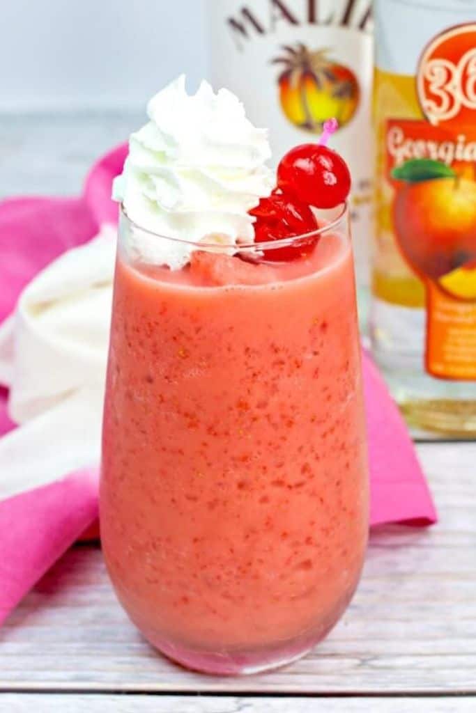 fruity pink cocktail in tall glass with whipped cream.