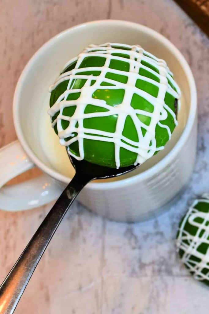 green hot cocoa bomb above mug of milk.
