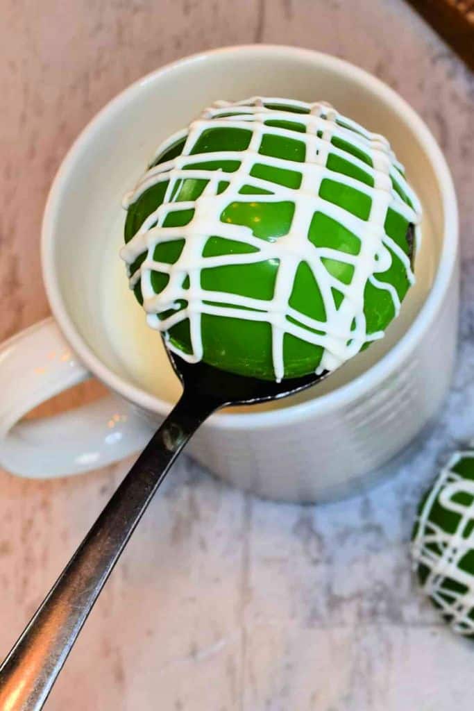 green hot cocoa bombs above mug of milk.