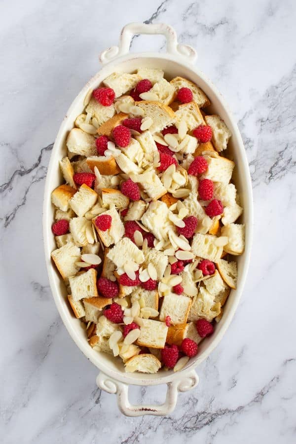 torn pieces of brioche with berries and almonds in dish.