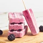 stack of blackberry fruit popsicles on wooden board with fresh blackberries.