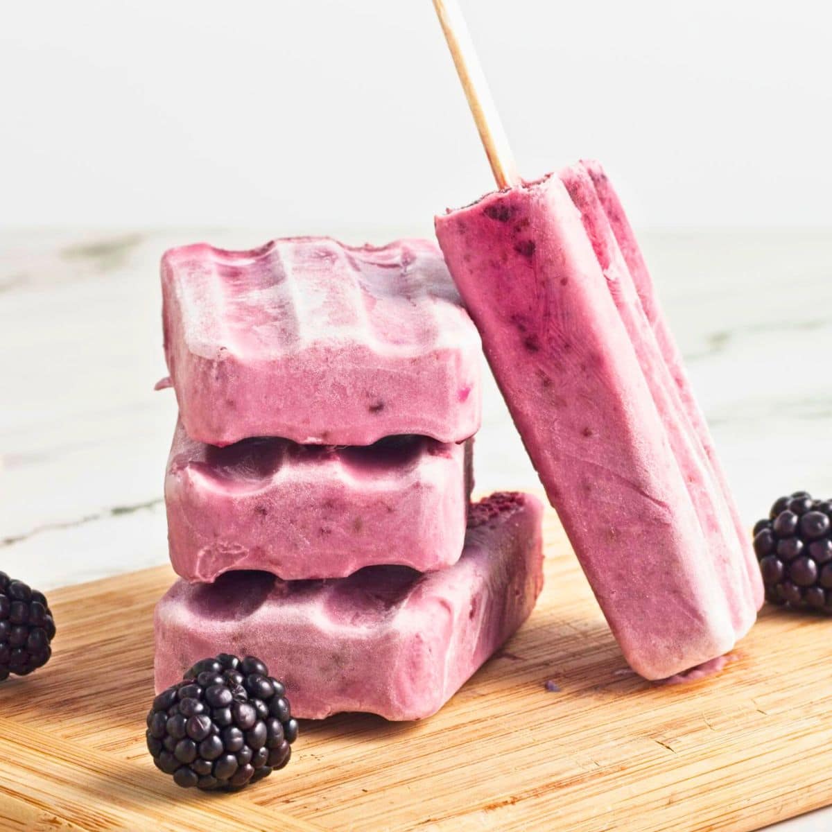 stack of blackberry fruit popsicles on wooden board with fresh blackberries.