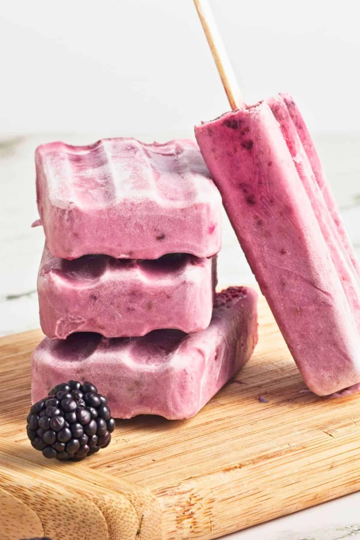 blackberry homemade popsicles stacked on wooden board.