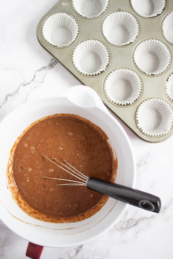 A bowl of cupcake batter with a whisk in it next to a muffin tin.