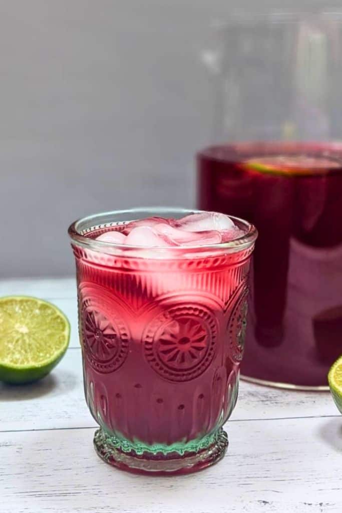 hibiscus limeade in glass with pitcher.