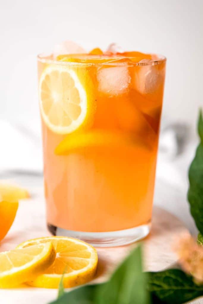 peach lemonade in glass with slice of lemon.