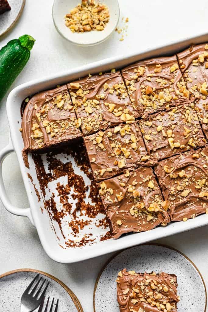 frosted chocolate zucchini cake in dish and topped with walnuts.
