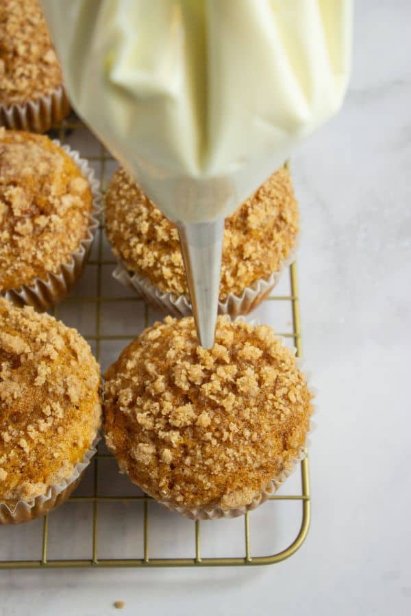 piping bag above pumpkin muffin on wire rack.