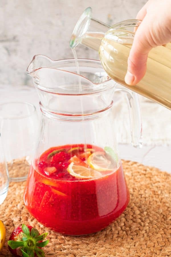 pouring simple syrup into pitcher of lemonade.