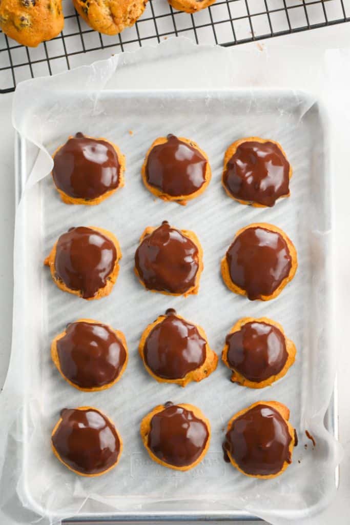 pumpkin cookies with chocolate ganache frosting on baking tray.