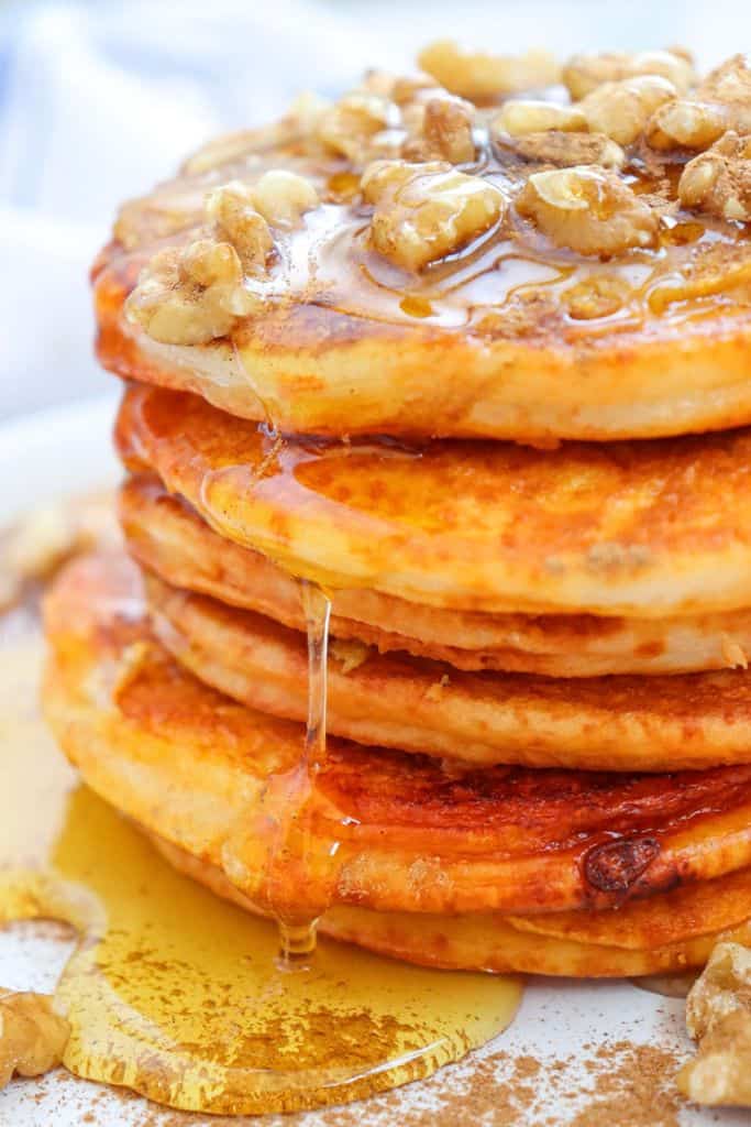 stack of pumpkin pancakes drizzled with syrup and walnuts.