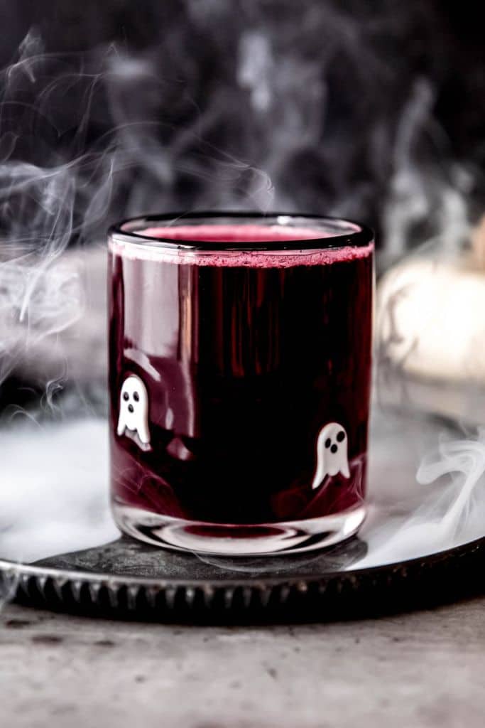dark red halloween lemonade in glass with white ghosts.