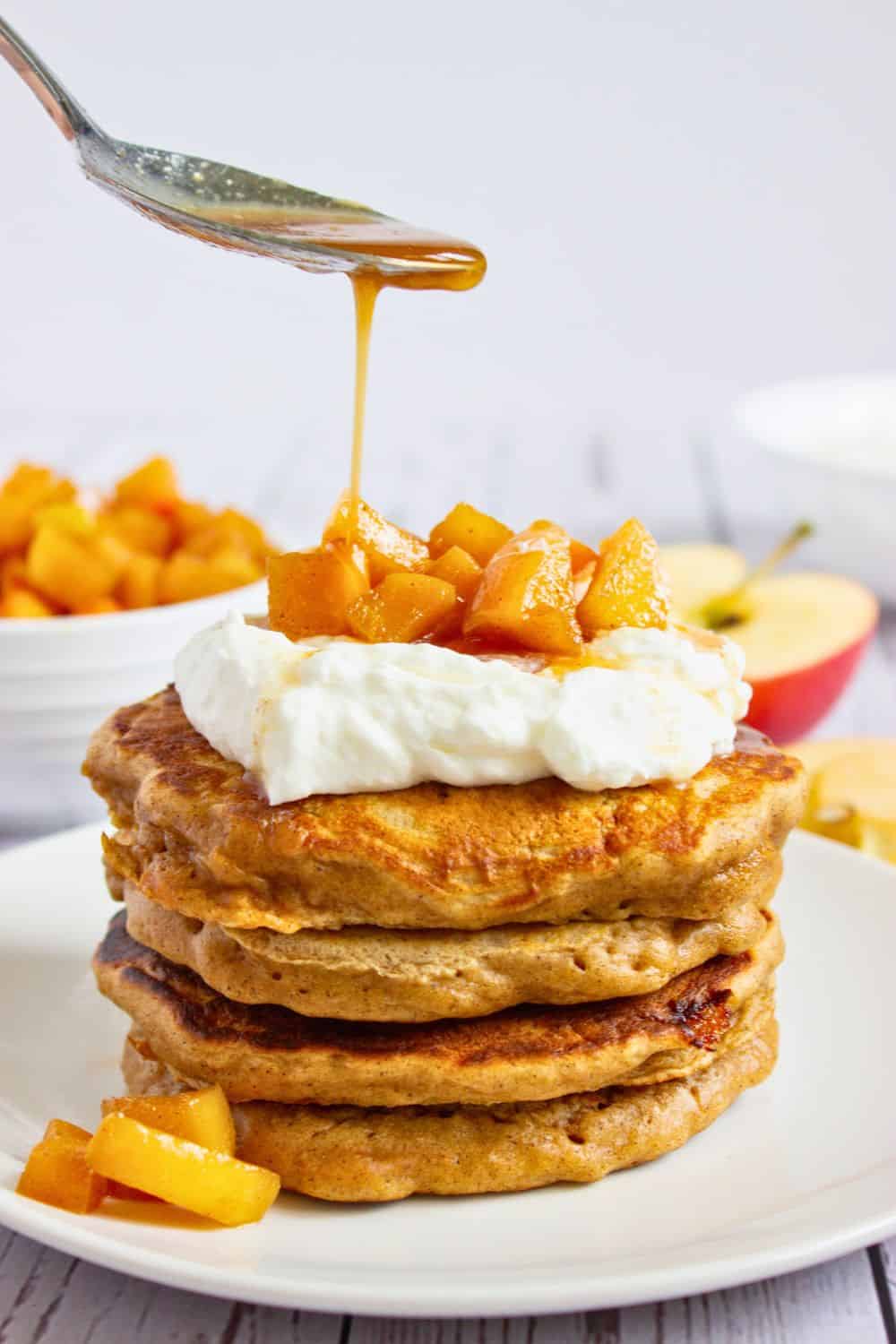 spoon drizzling caramel apple syrup over pancakes.