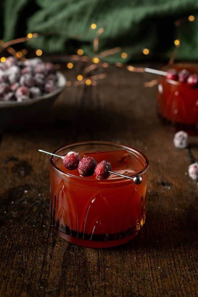 red thanksgiving mocktail in glass with sugared cranberries.