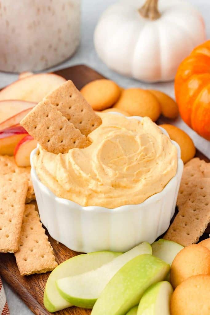 bowl with pumpkin dip surrounded by crackers and fresh fruit dippers.