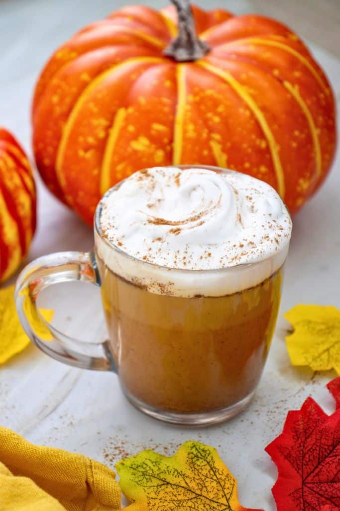 pumpkin spice latte topped with foam in glass mug.