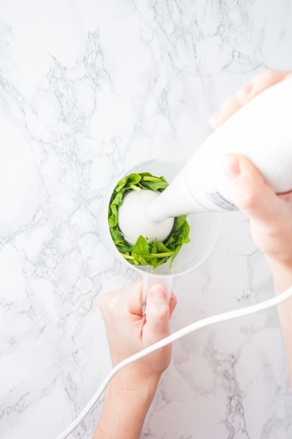 stick blender in bowl of fresh spinach to puree.