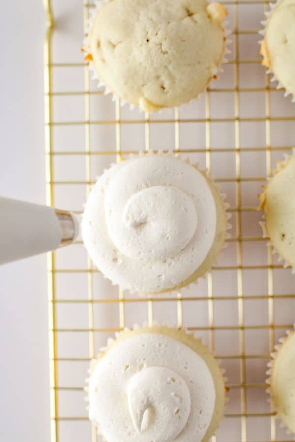 adding frosting to white chocolate cupcakes on wire rack.